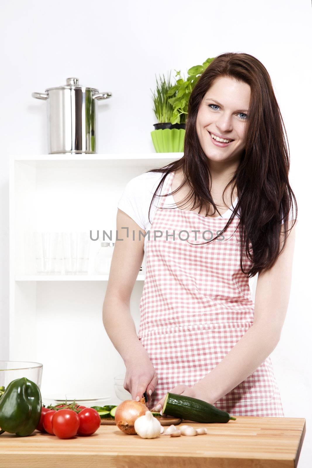 happy young woman in a kitchen cutting cucumber for salad