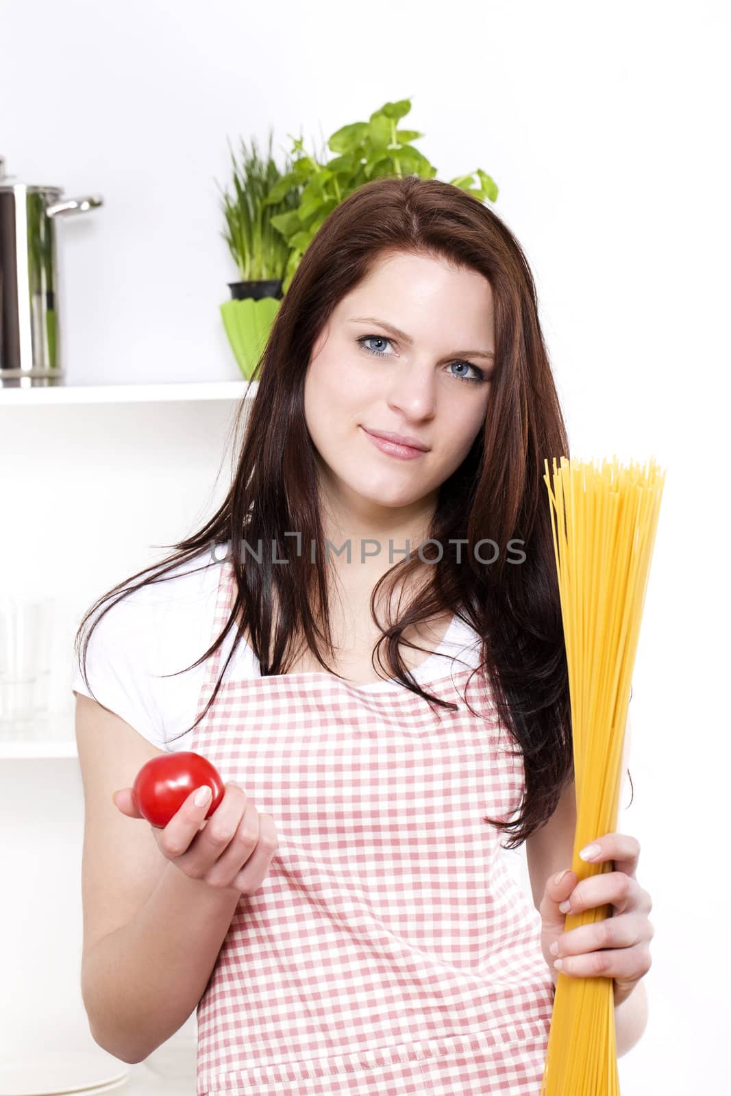 smiling young woman in a kitchen holding spaghetti and tomato