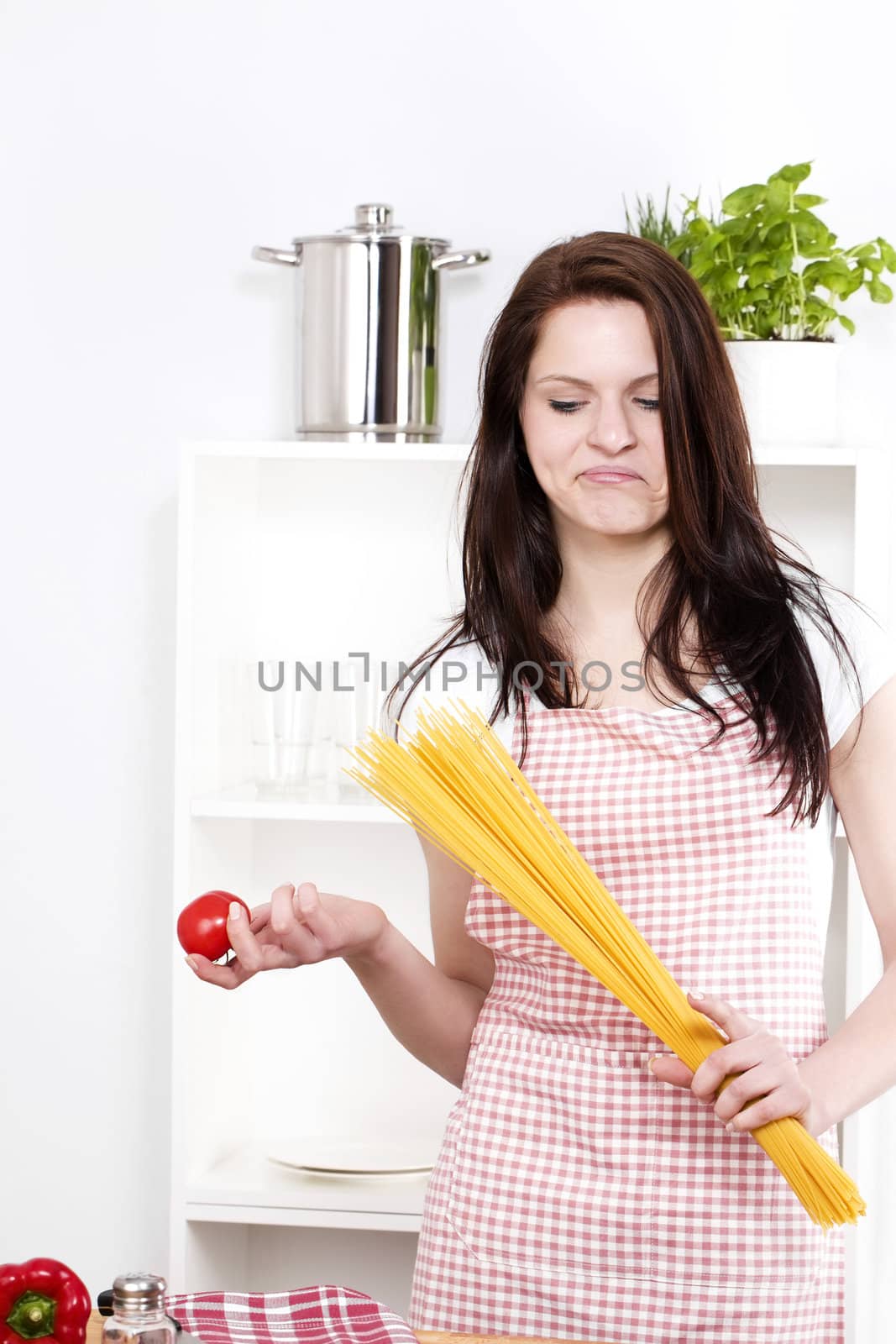 young woman holding pasta and tomato looking at the tomato in her hand