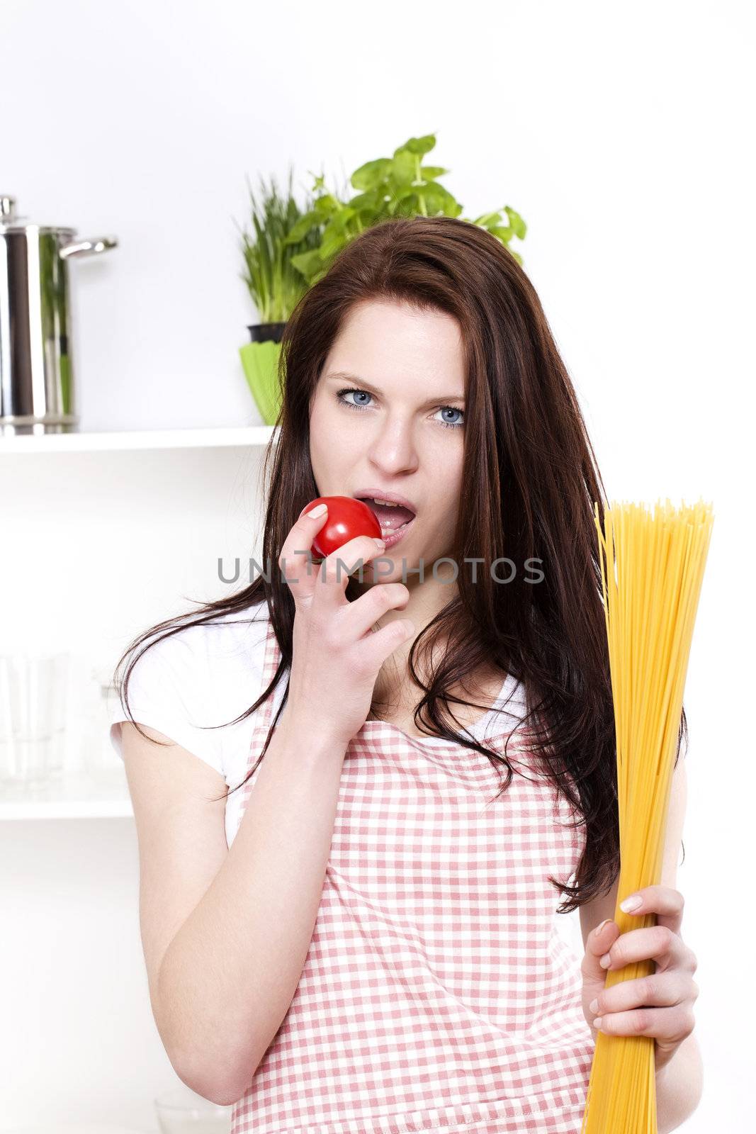 young woman holding pasta and tomato about to eat the tomato