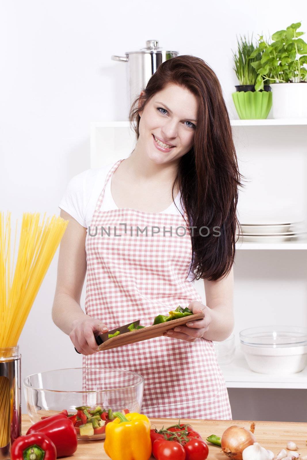 happy smiling young woman in a kitchen adding chopped paprika to her salad in a bowl