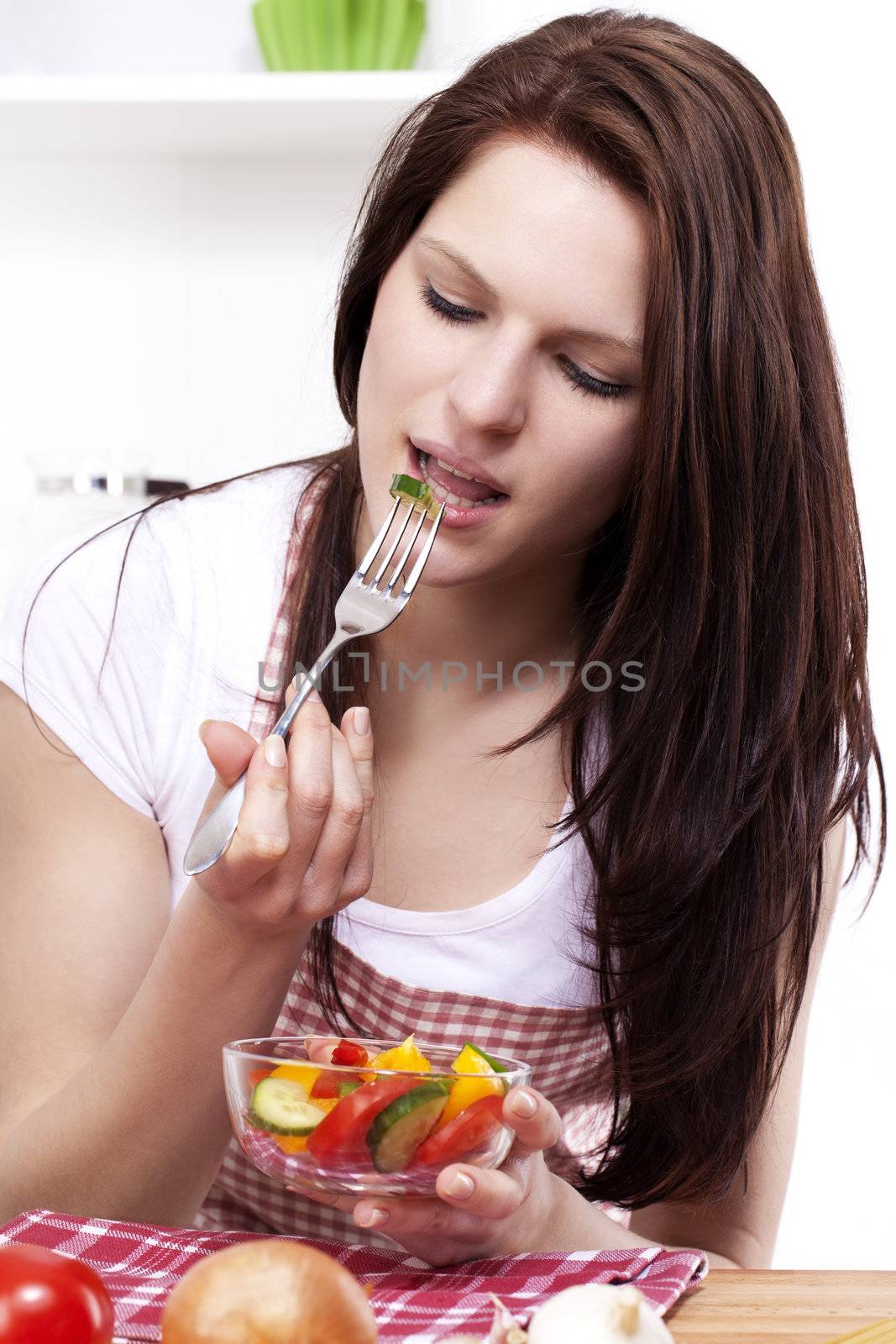 young woman in kitchen eating mixed salad from a small bowl