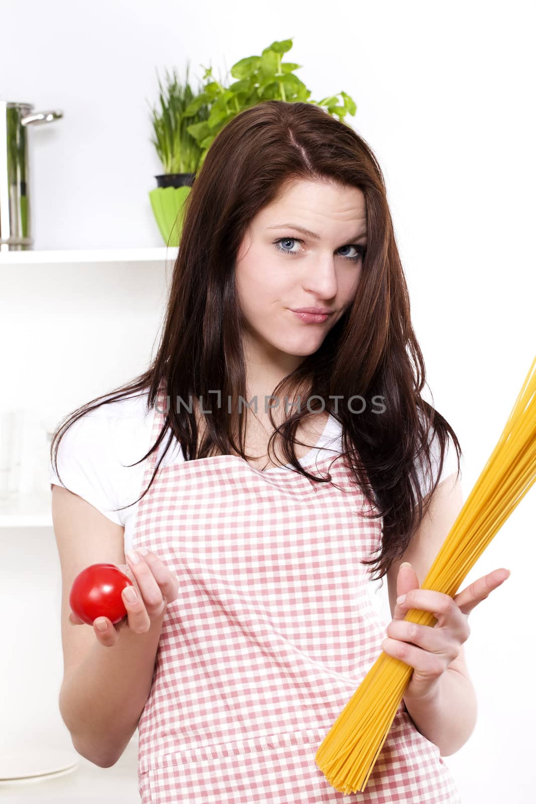 young smiling woman in a kitchen holding tomato and spaghetti