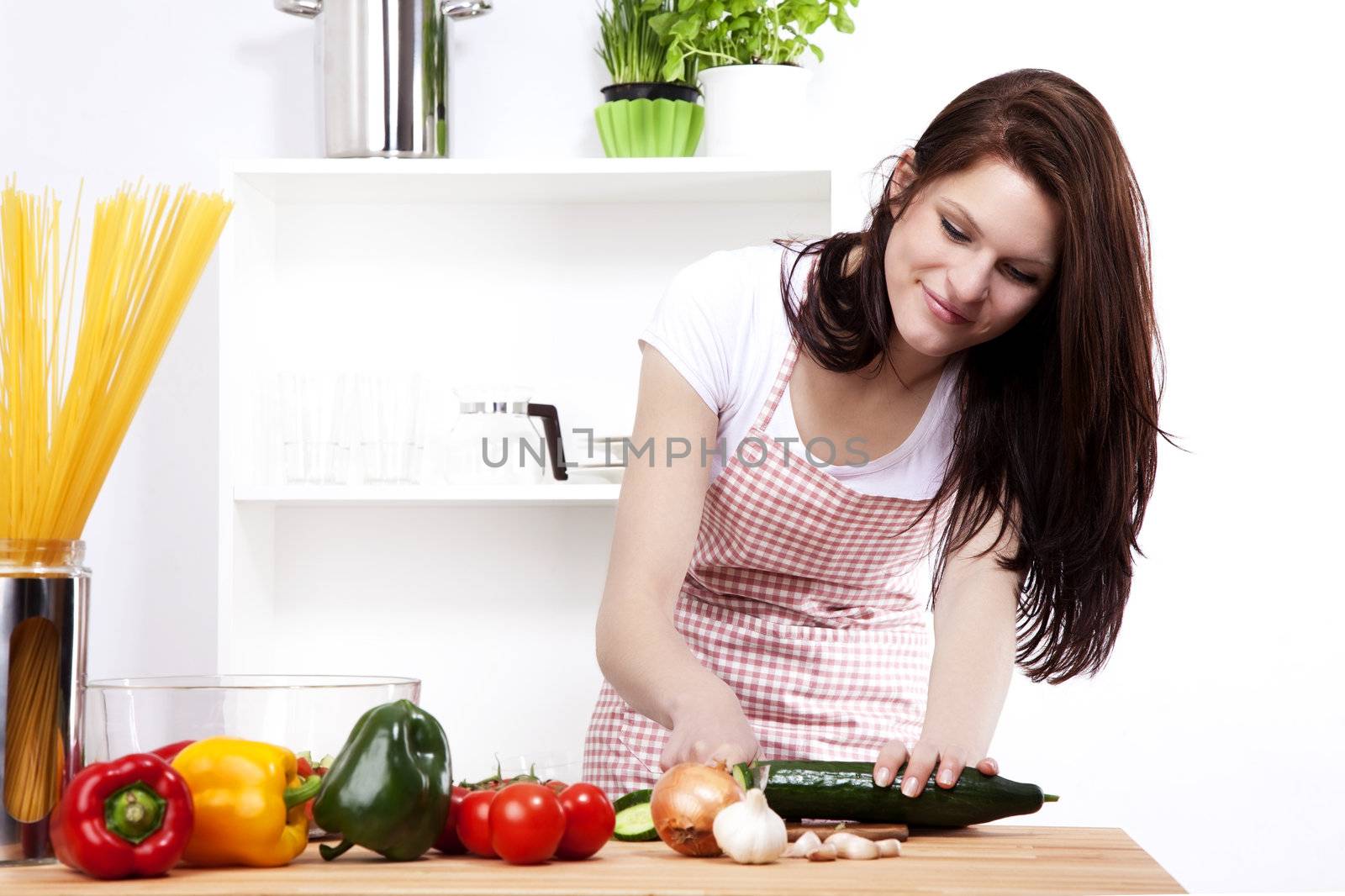 young happy woman in a small kitchen chopping cucumber for salad
