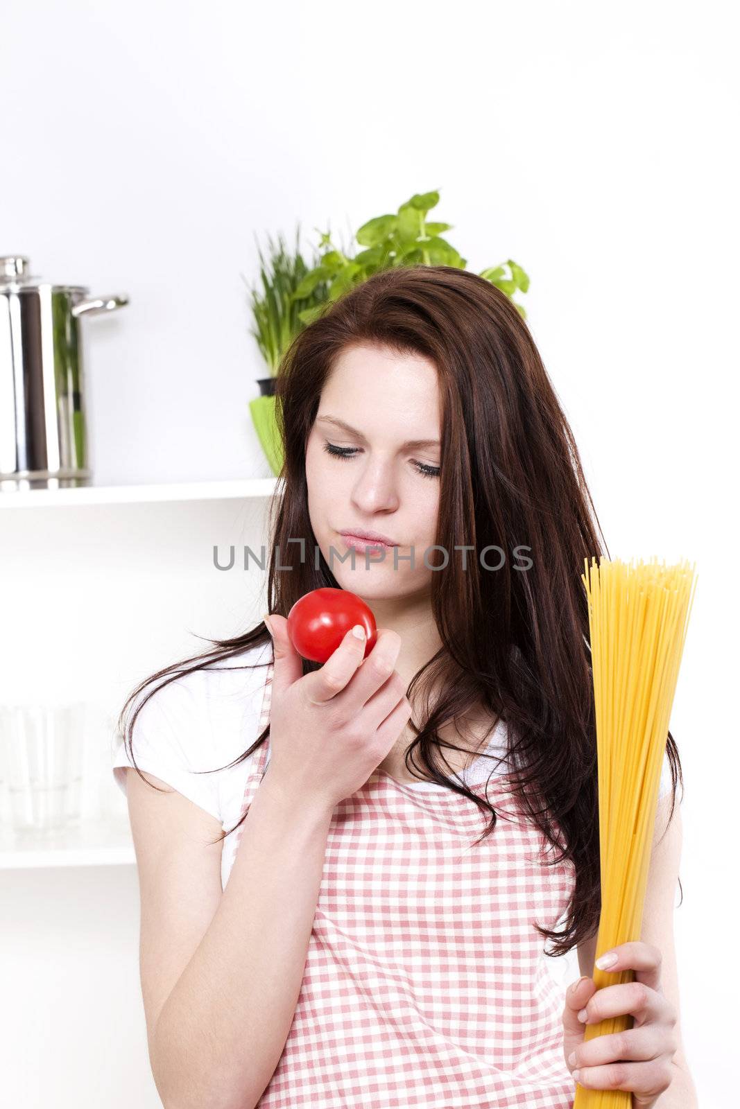 young pretty woman looking at a tomato holding spaghetti