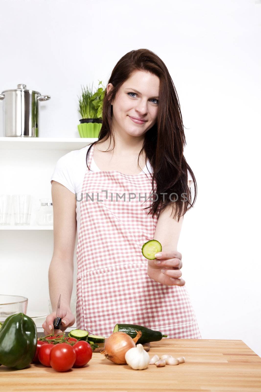 young happy woman in her kitchen offering a piece of cucumber