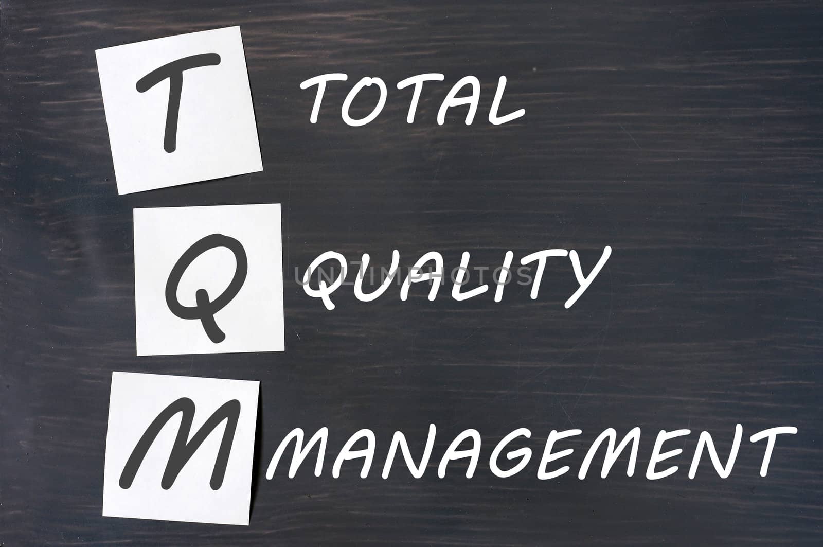 Acronym of TQM for total quality management - white chalk handwriting and sticky notes on a blackboard 