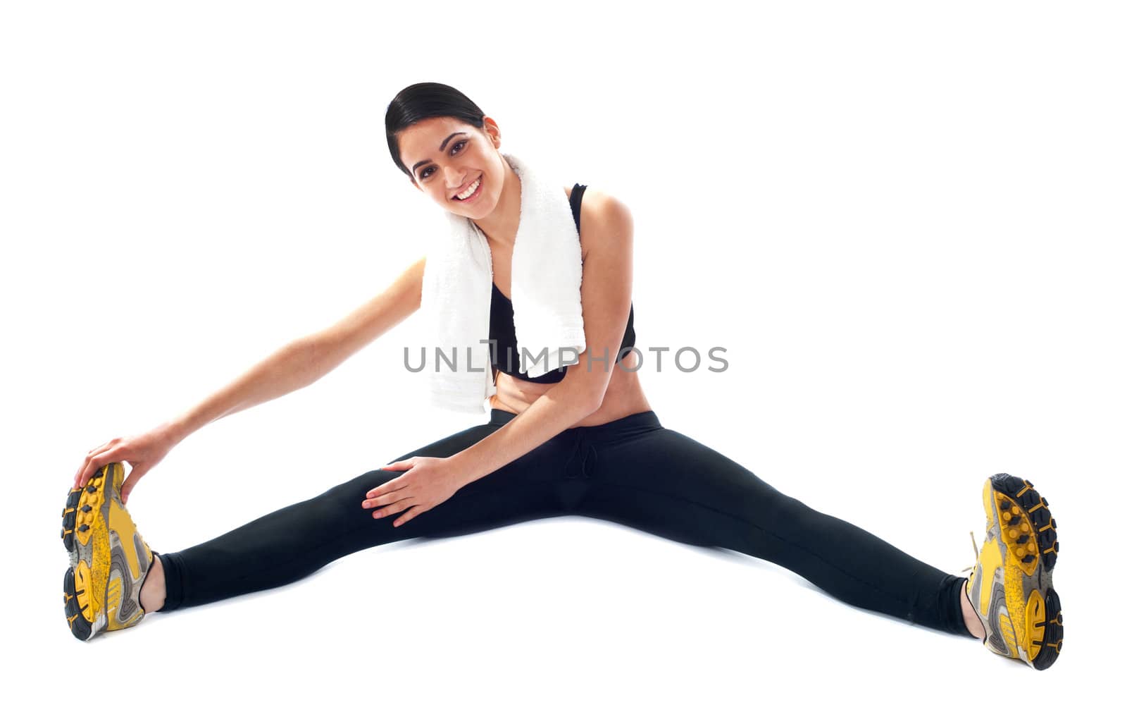 Young fit female trainer doing stretching on floor against white background