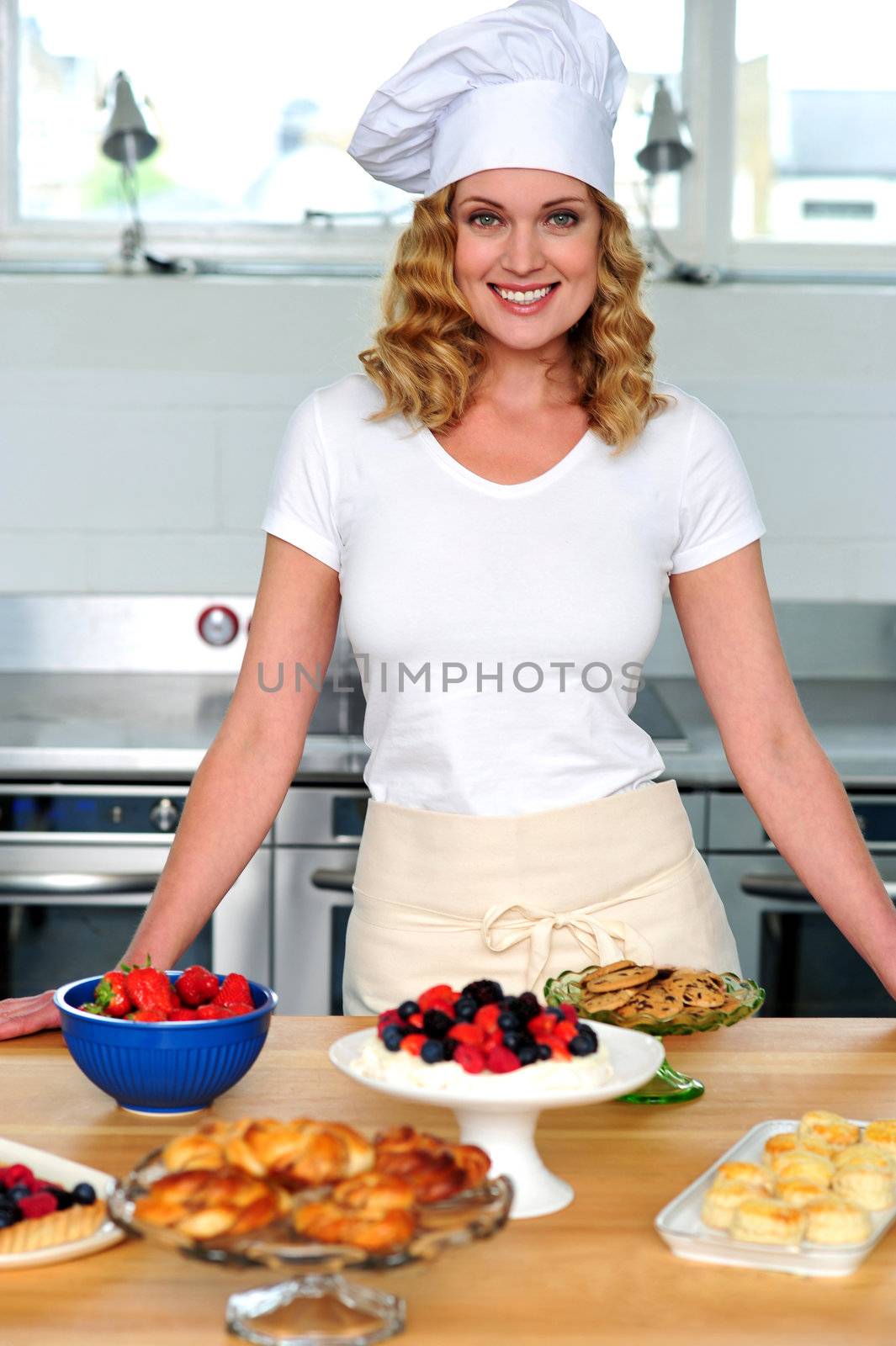 Female chef posing in uniform inside kitchen. Yummy snacks ready on the table