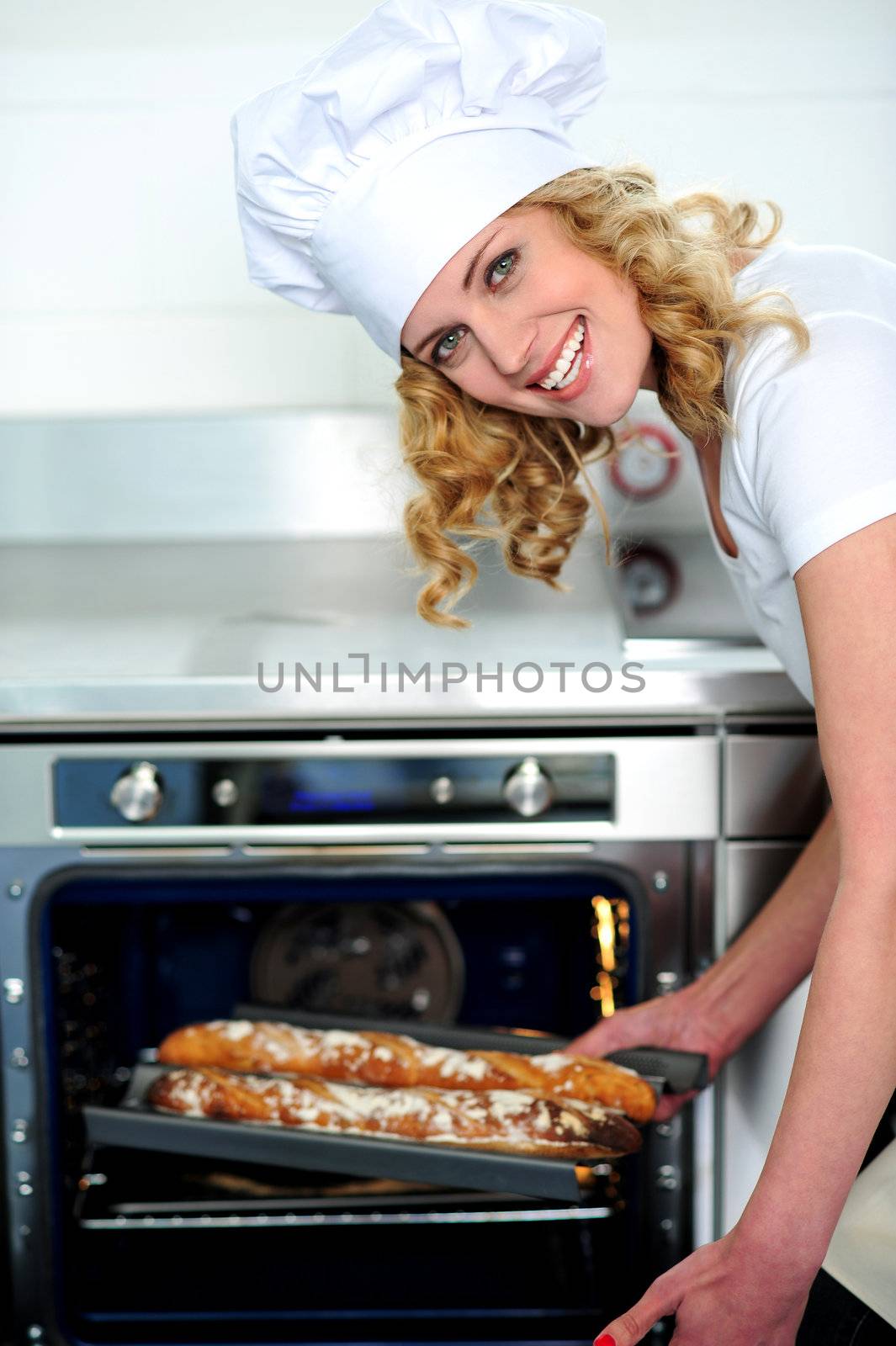 Female chef taking out baguette from oven. Bent down
