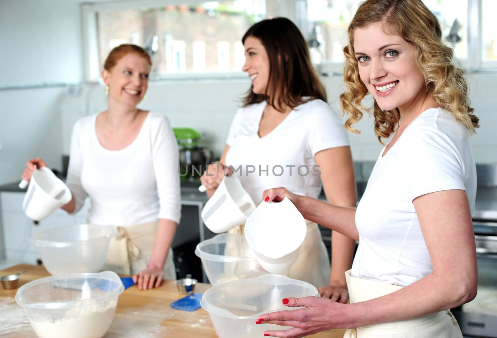Female bakers pouring water into a plastic bowl containing dough mixture