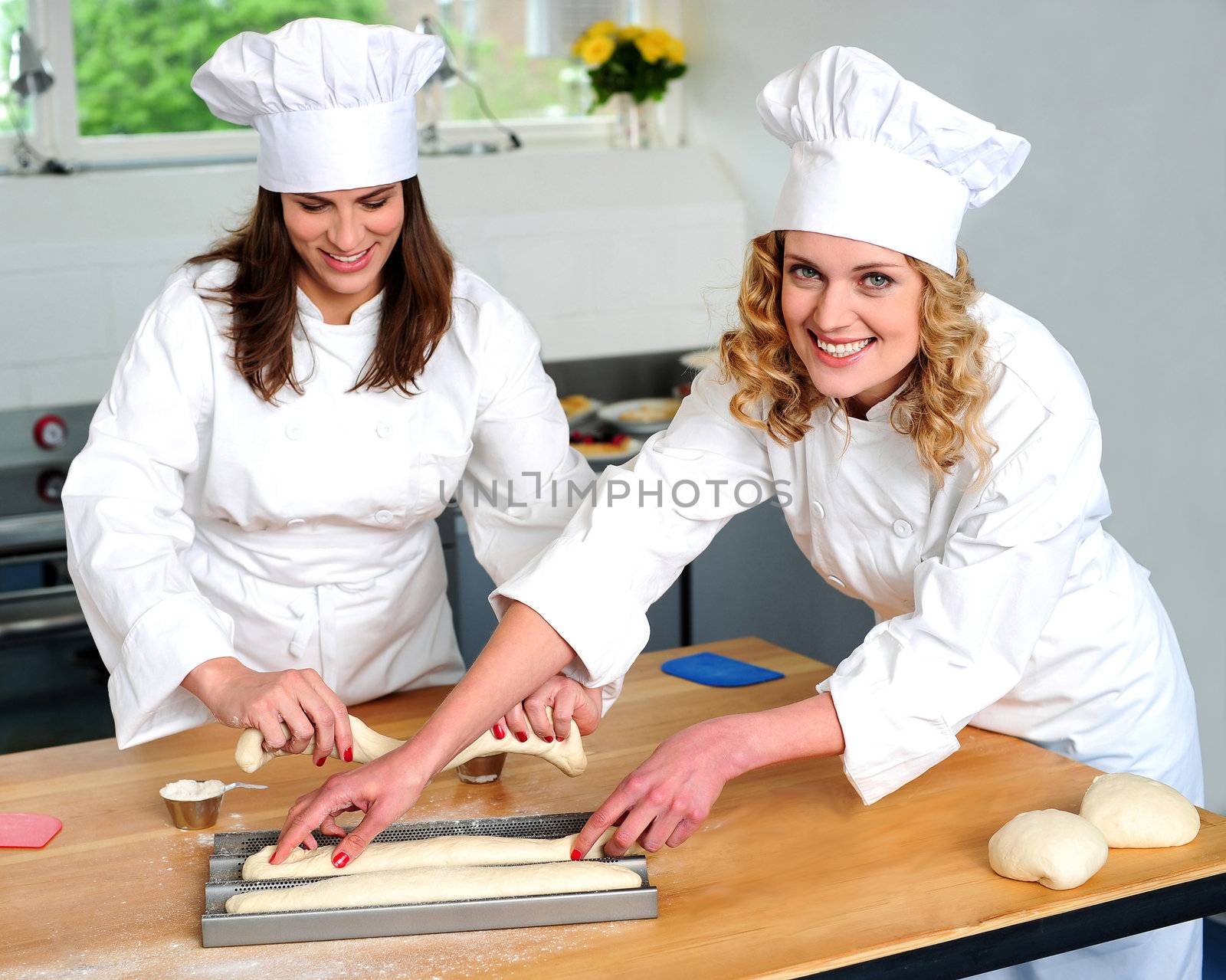 Female chef arranging prepared dough in racks. Other chef making long rolls