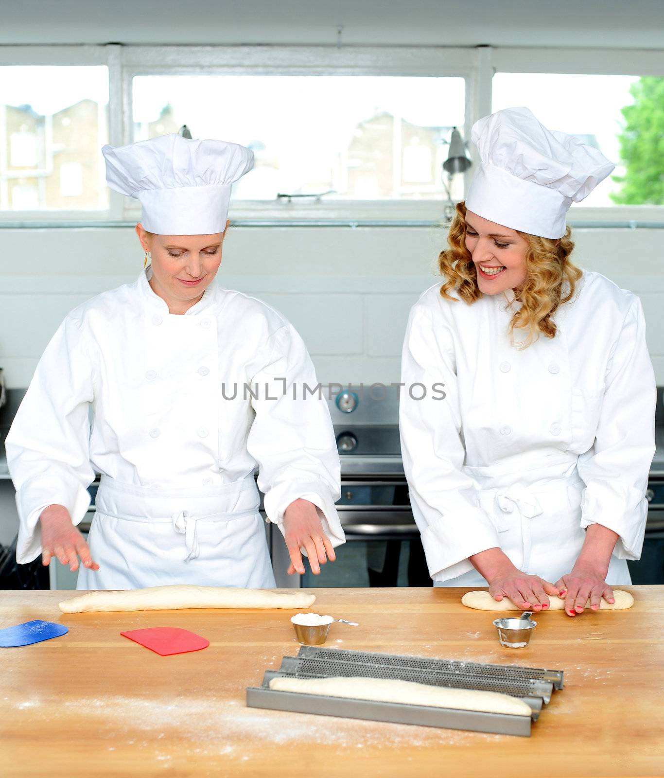 Senior chef teaching newbie female chef, how to roll and knead dough