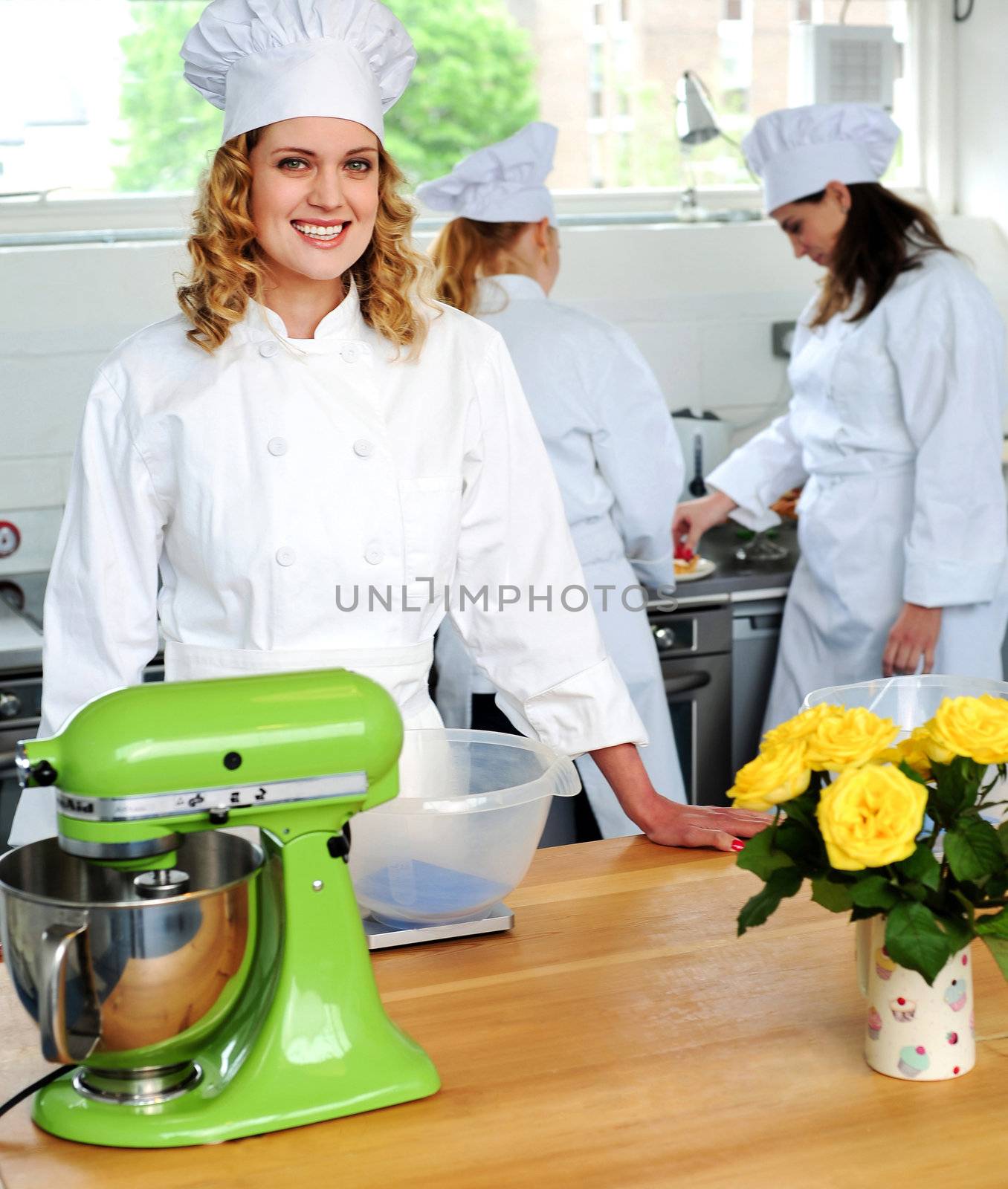 Two chefs working in background while third chef in focus looking at camera and smiling
