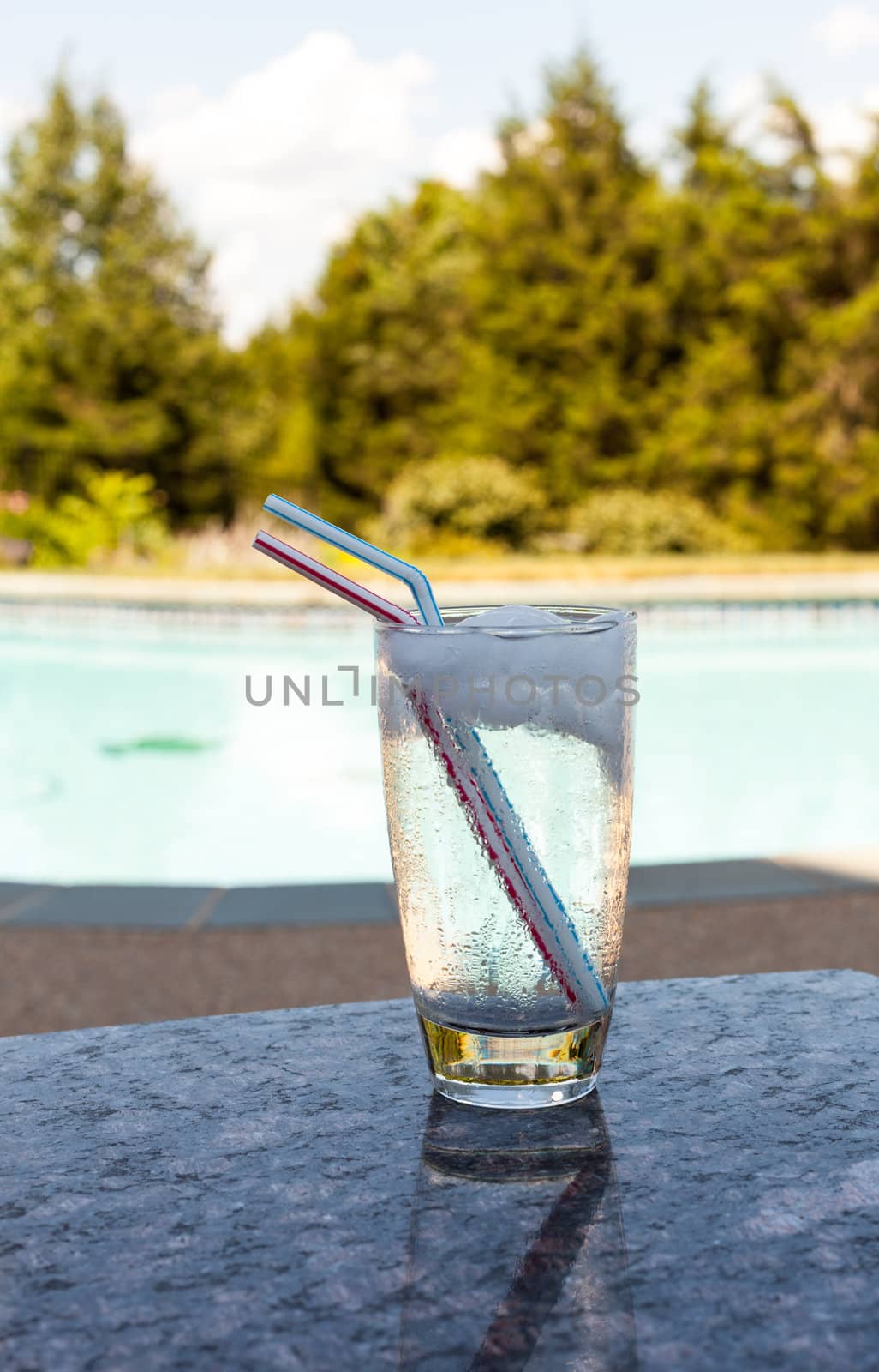Plain glass of water with ice cubes on side of blue swimming pool