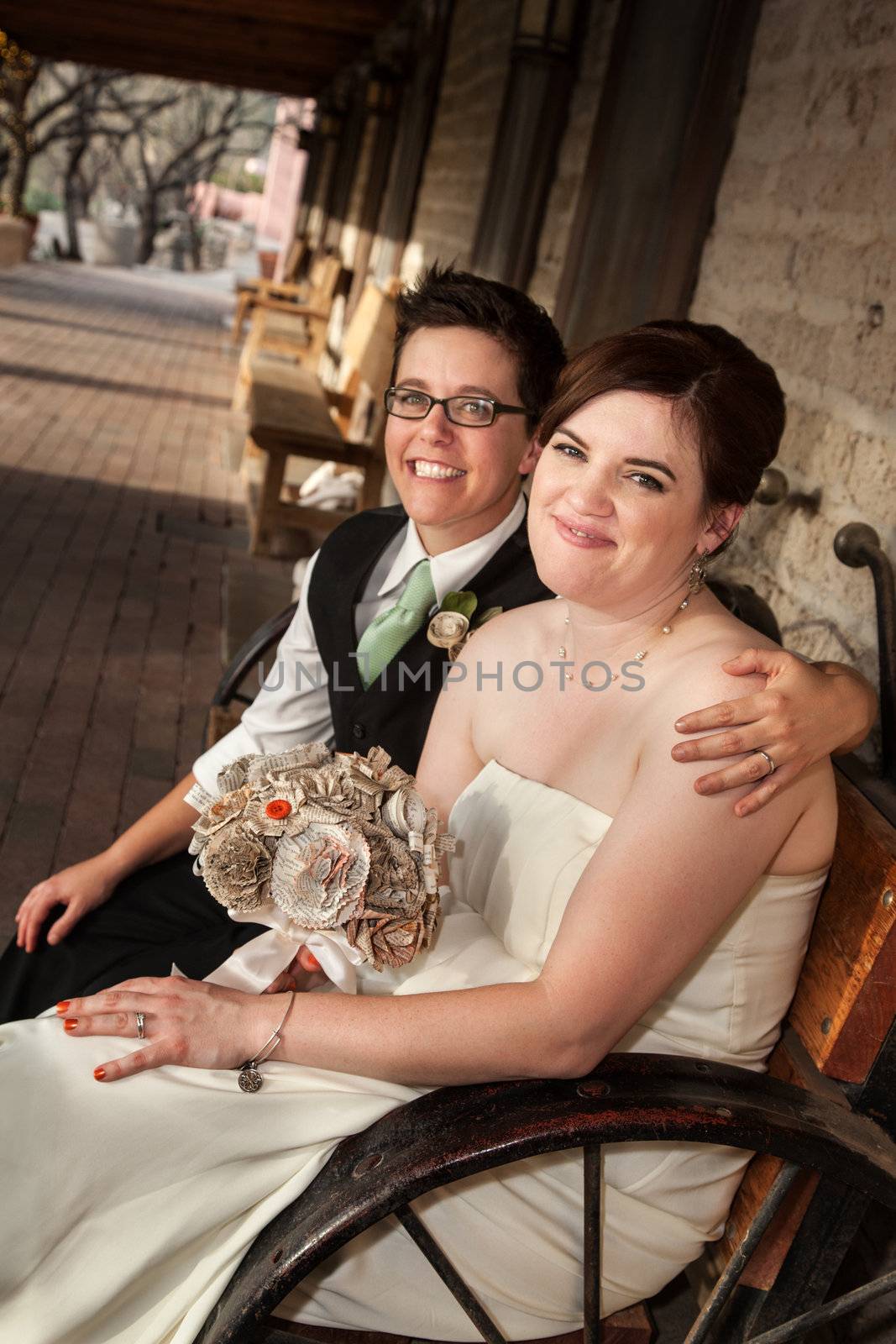 Caucasian lesbian newlyweds sitting on rustic bench