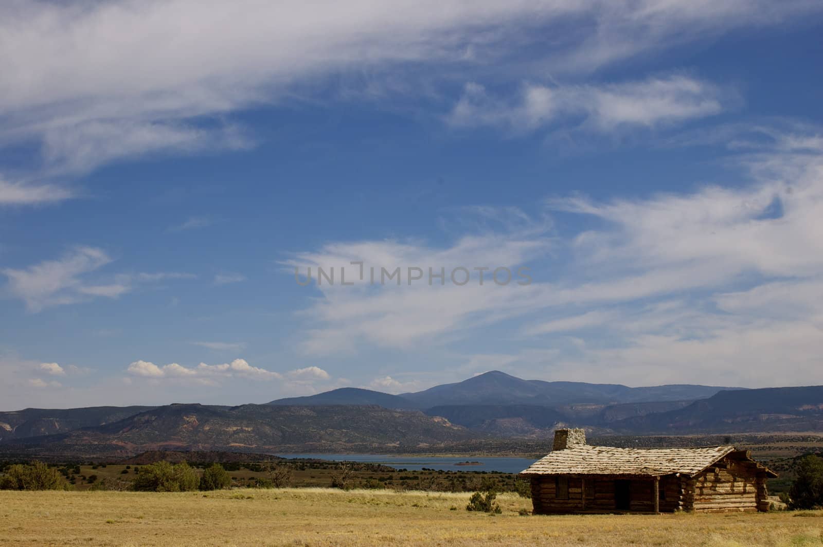 Rustic 'wild west' style log cabin against a blue sky, mountains and desert with copy space.