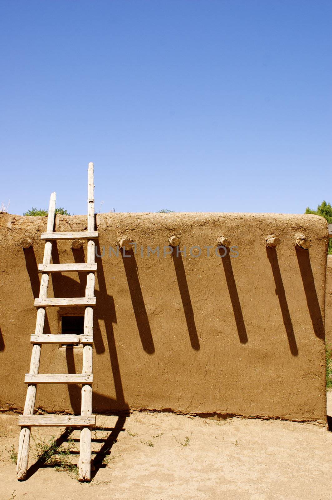 New Mexican Adobe Pueblo Building, featuring a ladder and shadows, on a native American Indian reservation (outside Taos), against a deep blue sky with copy space.