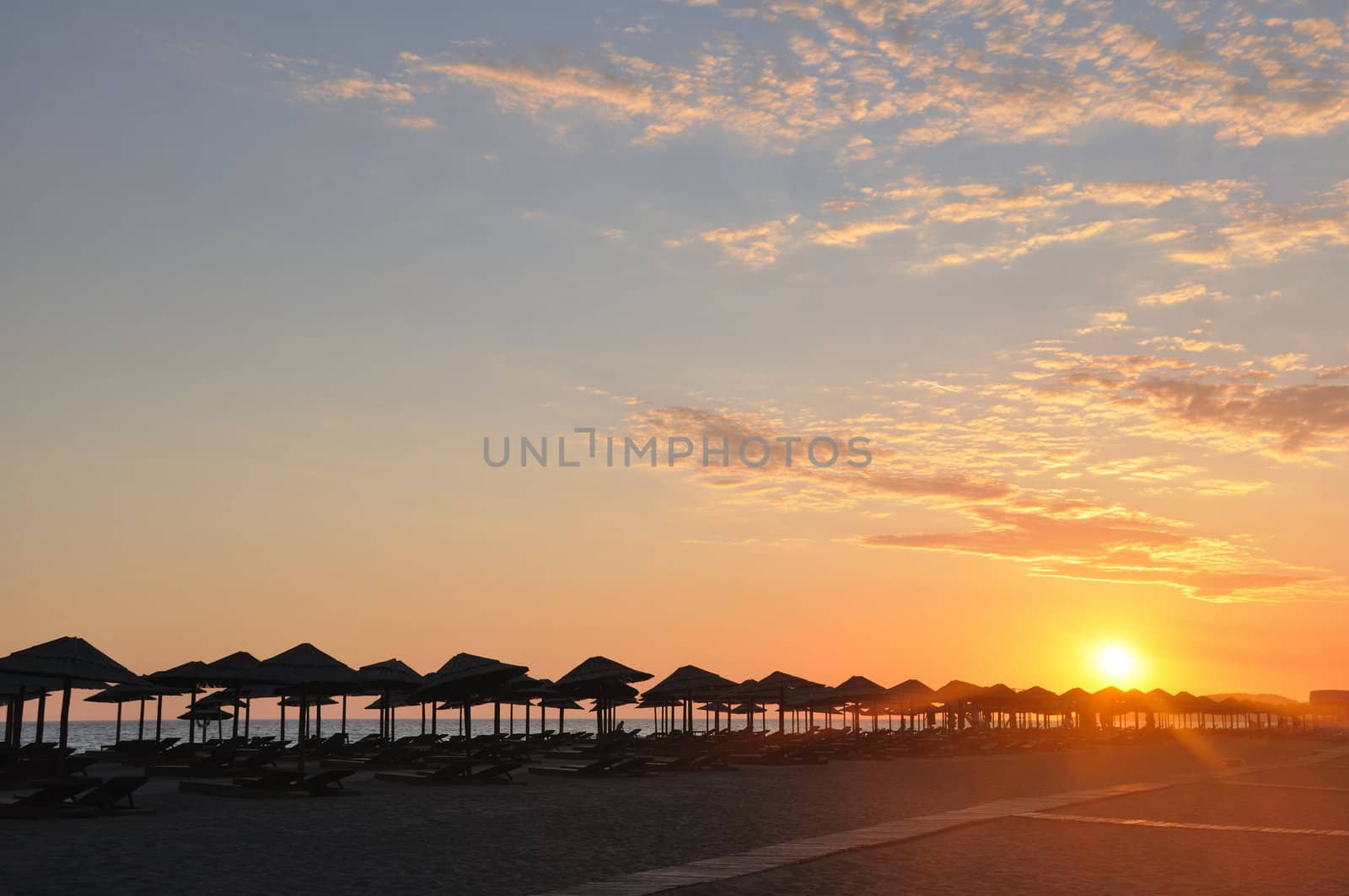 Umbrella on sandy sea beach at sunset stock photo