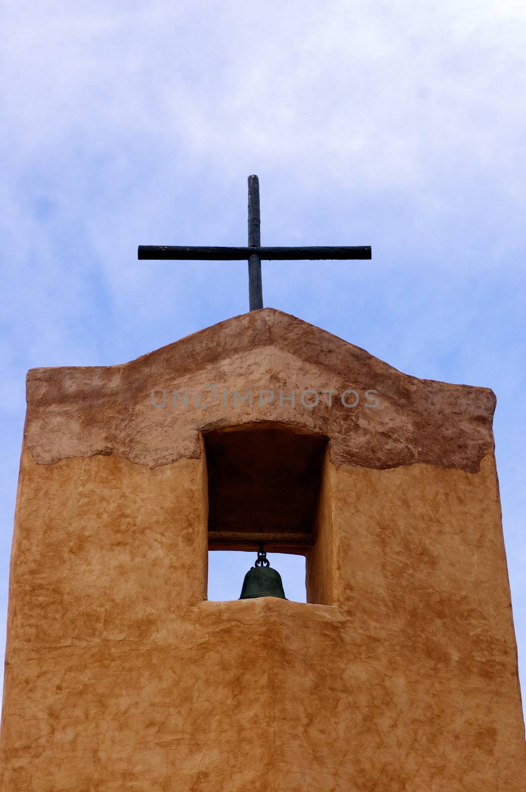 New Mexican Adobe Church bell tower with cross, against a blue sky with copy space.