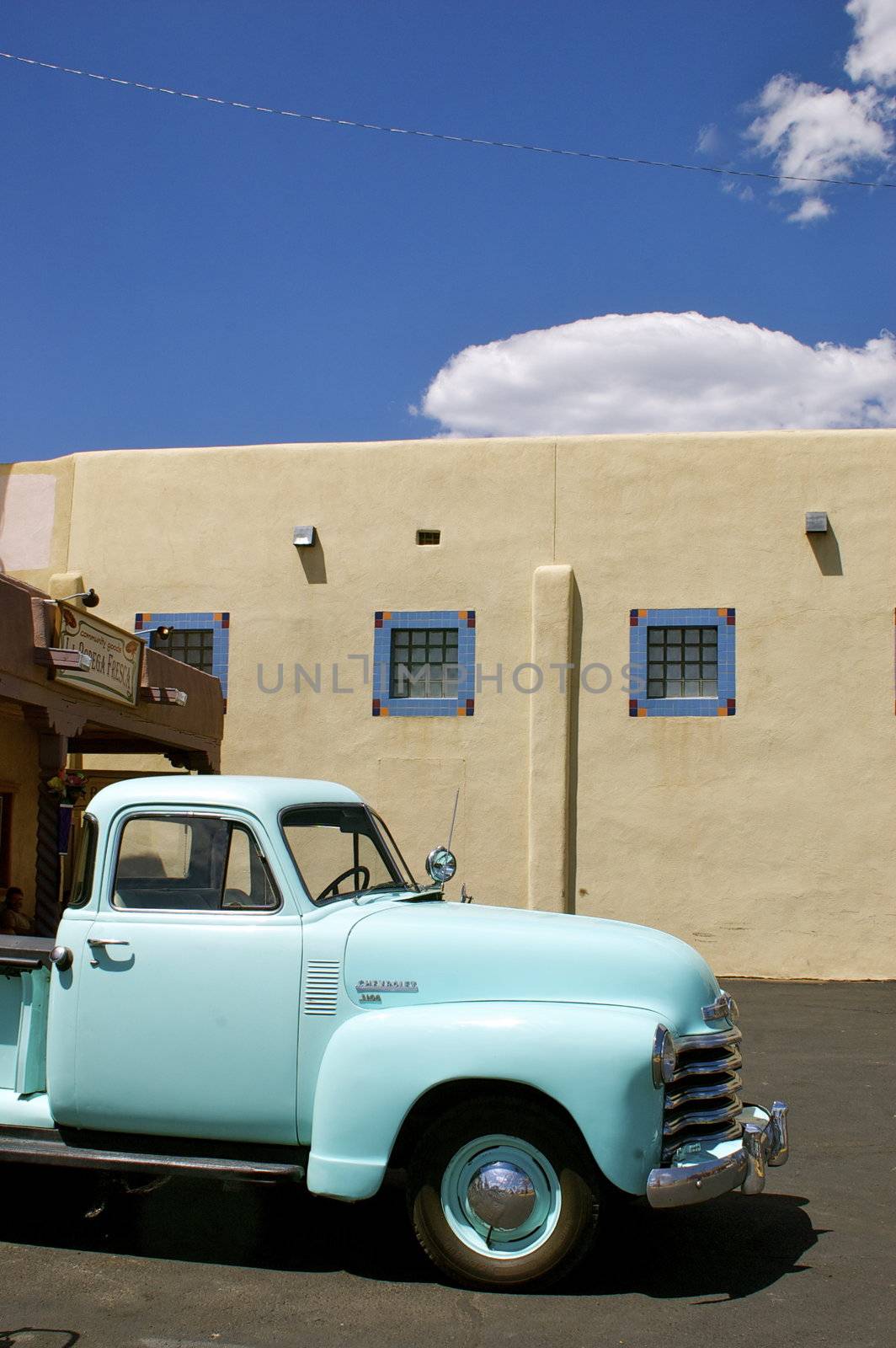Vintage blue truck parked in front of an adobe building against a blue sky with copy space.