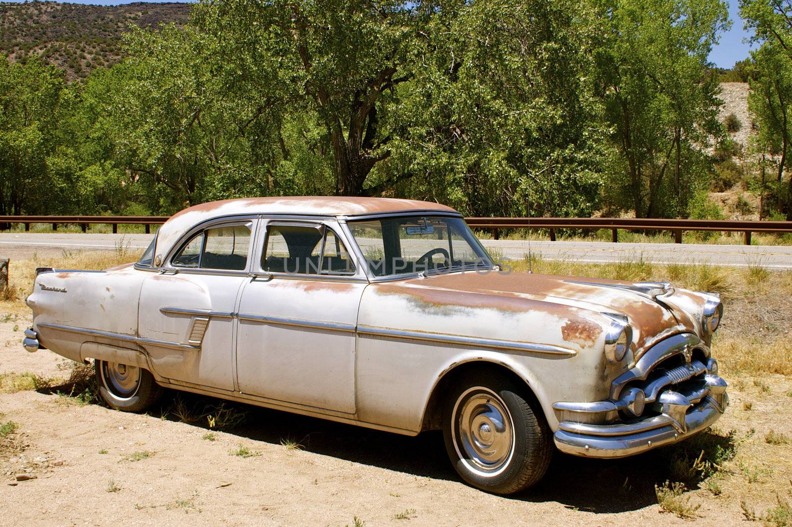 Rusting vintage American car (Packard), taken along the side from the front, parked outdoors.