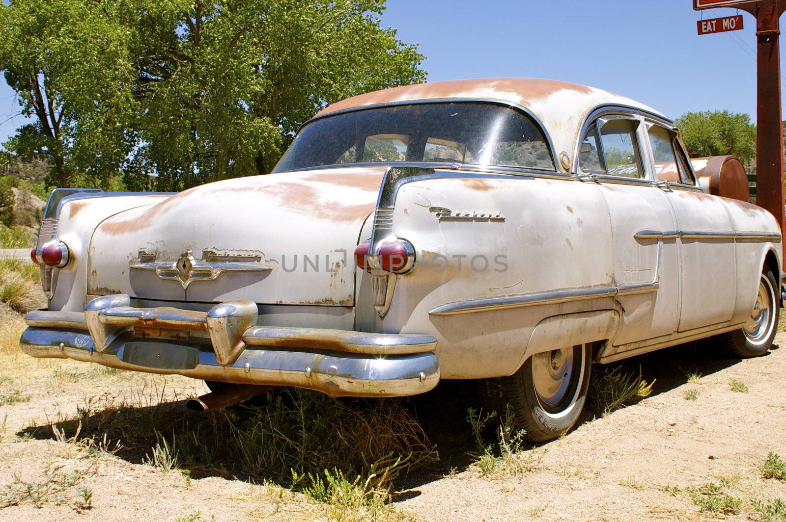 Rusting vintage American car (Packard), taken along the side from the back, parked outdoors.