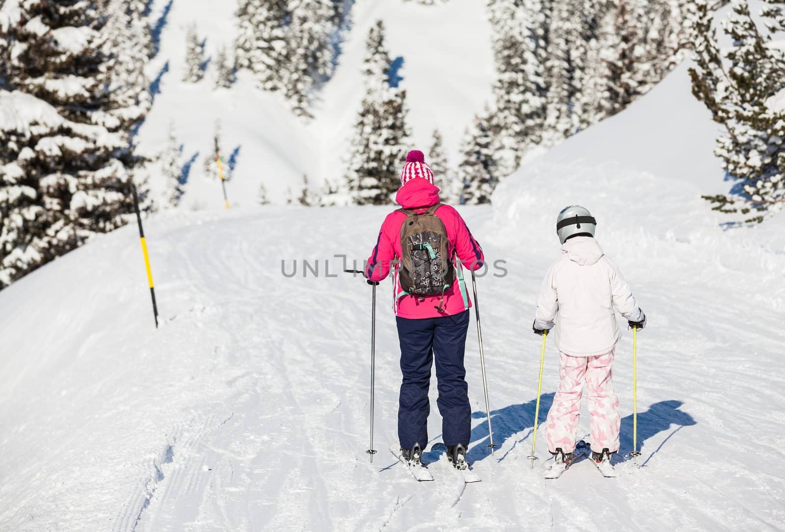 Back view of girl in ski goggles and a helmet with his mother, Zellertal, Austria. Vertical view