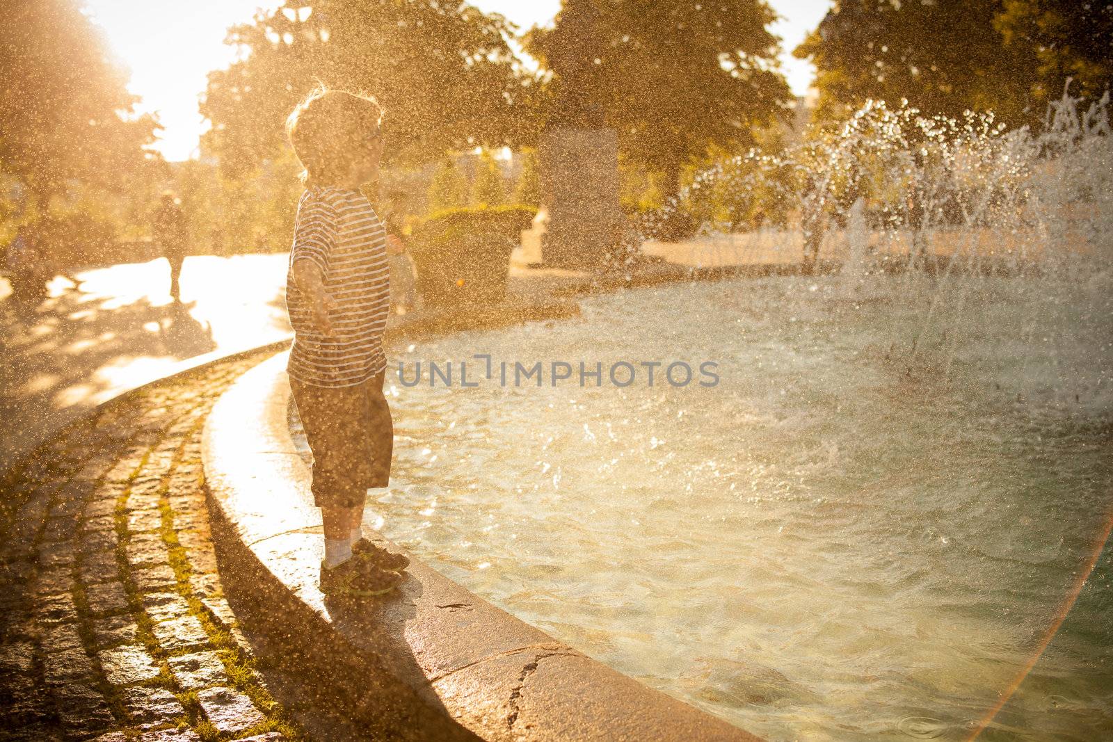 Boy standing by a fountain at sunset and getting wet