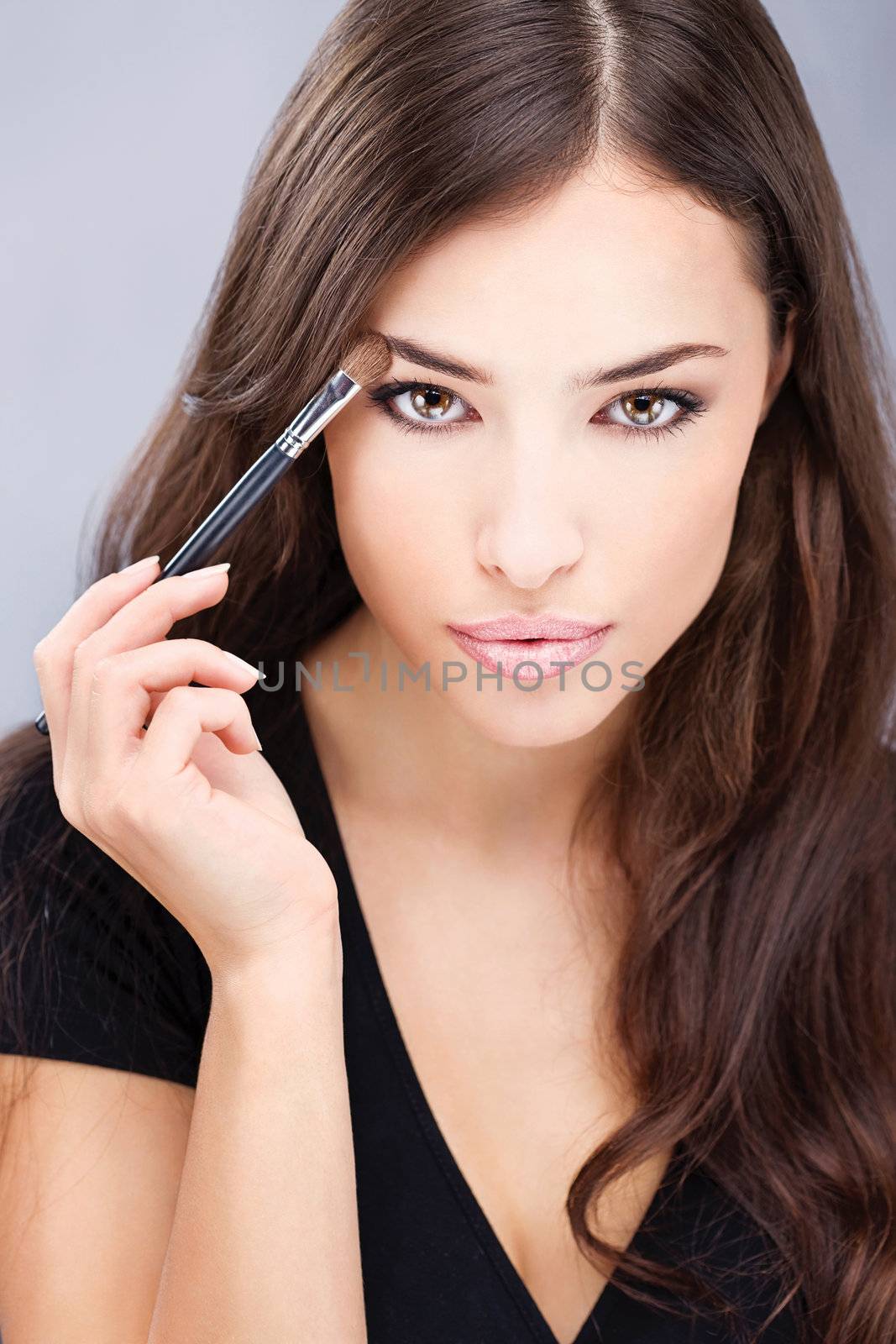 pretty black hair woman applying make up with brush in her right hand