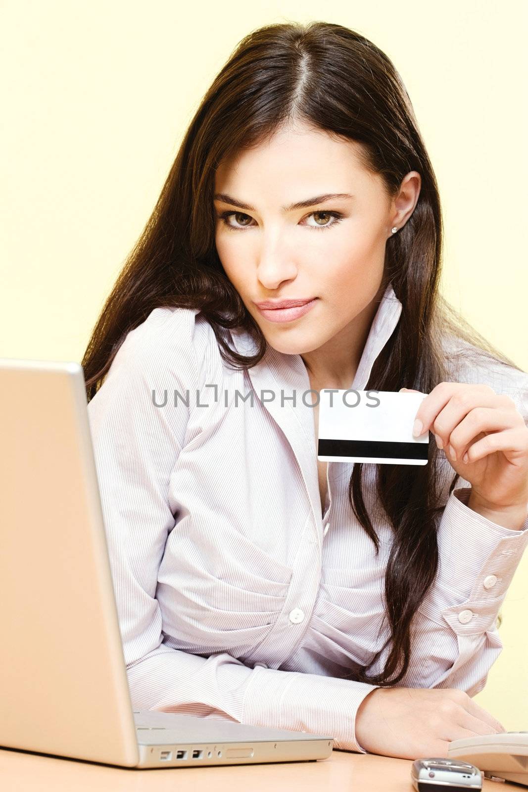 Beautiful young woman sitting near laptop and mobile phone holding credit card in her left hand
