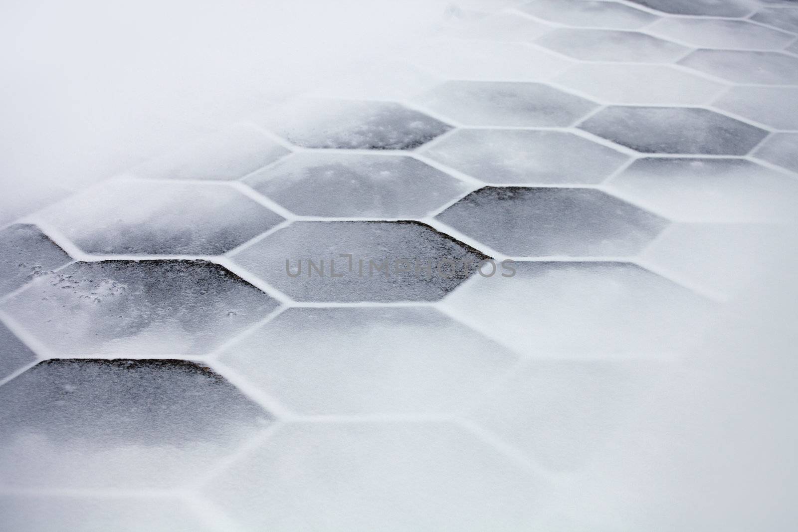 Hexagonal sidewalk tiles covered with snow and ice