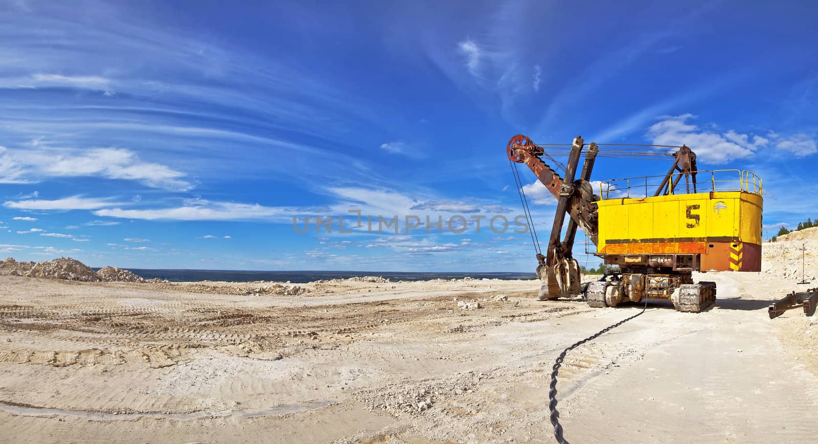 Heavy excavator in quarry for the extraction of gravel. Against the background of blue sky.