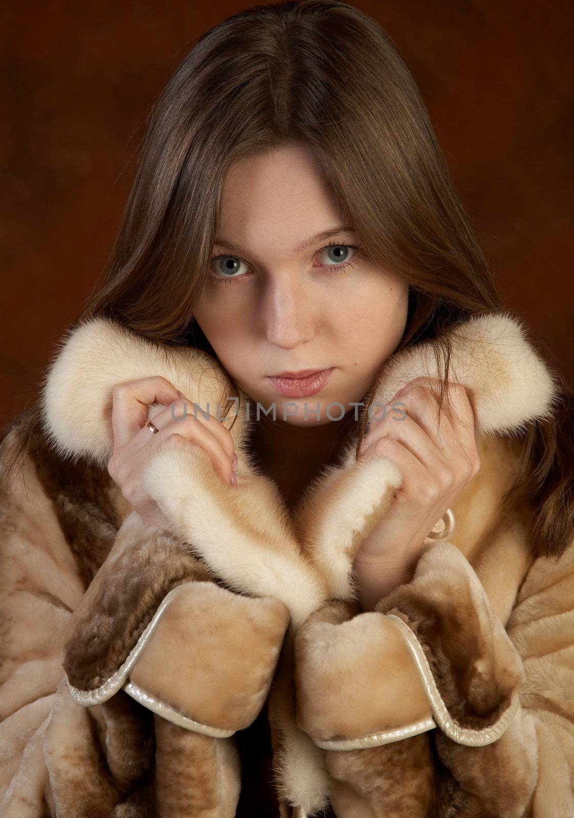The girl in a fur coat on motley background in studio
