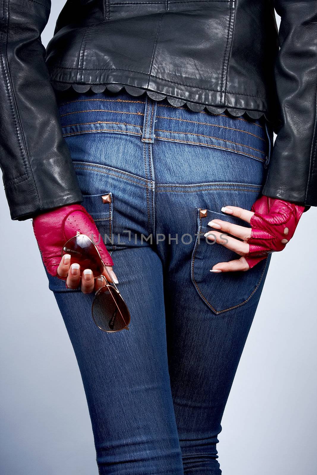 Women's hands with the sunglasses in stylish gloves back on the background of jeans