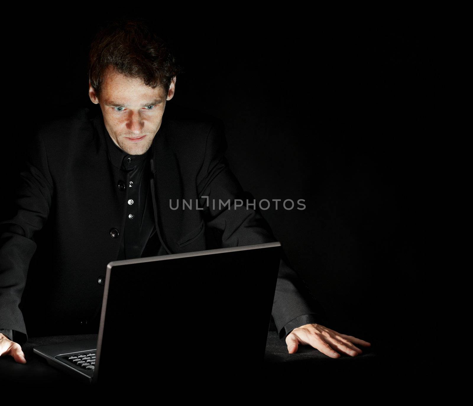 Hacker with laptop in dark room by pzaxe