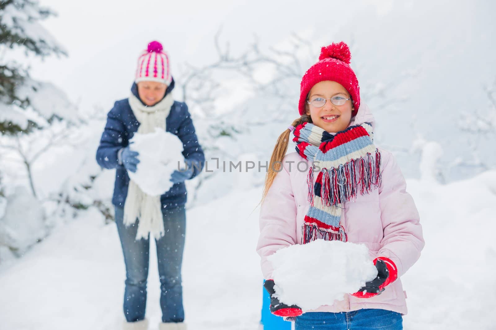 Smiling happy girl with her mother having fun outdoors on snowing winter day in Alps playing in snow.