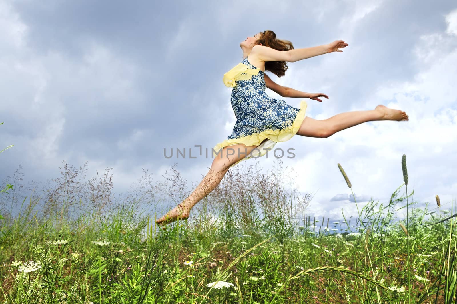 Young teenage girl jumping in summer meadow amid wildflowers