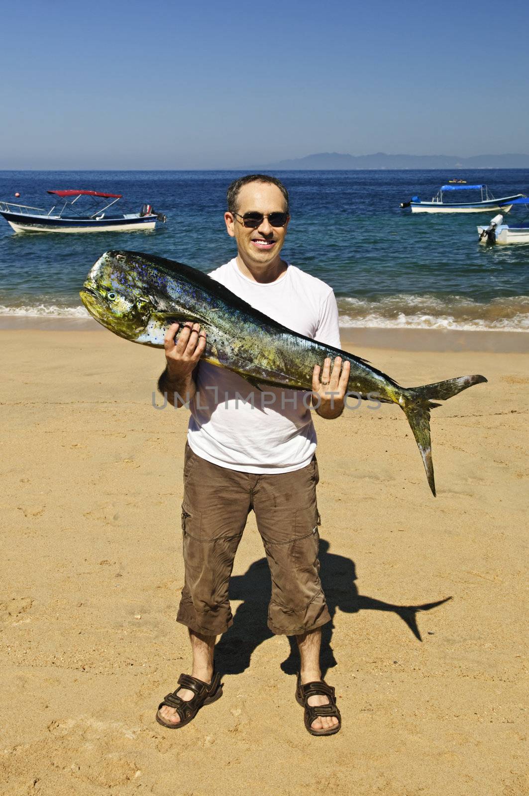 Tourist holding big fish on beach by elenathewise