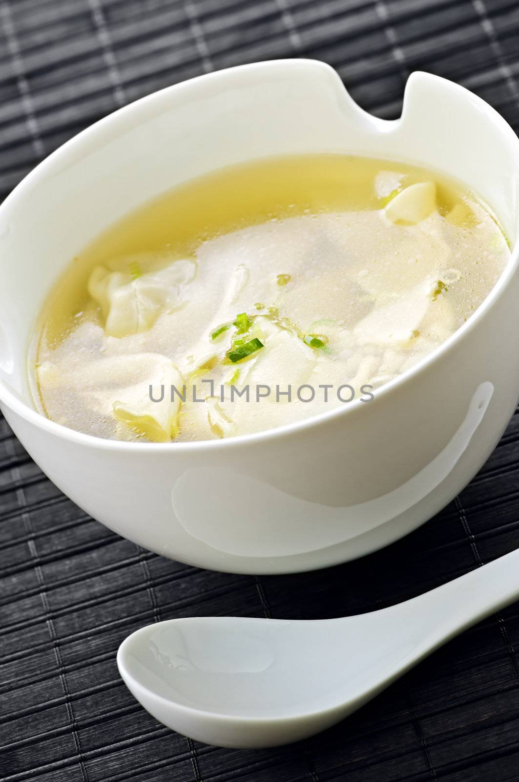 Wonton soup in white bowl with spoon