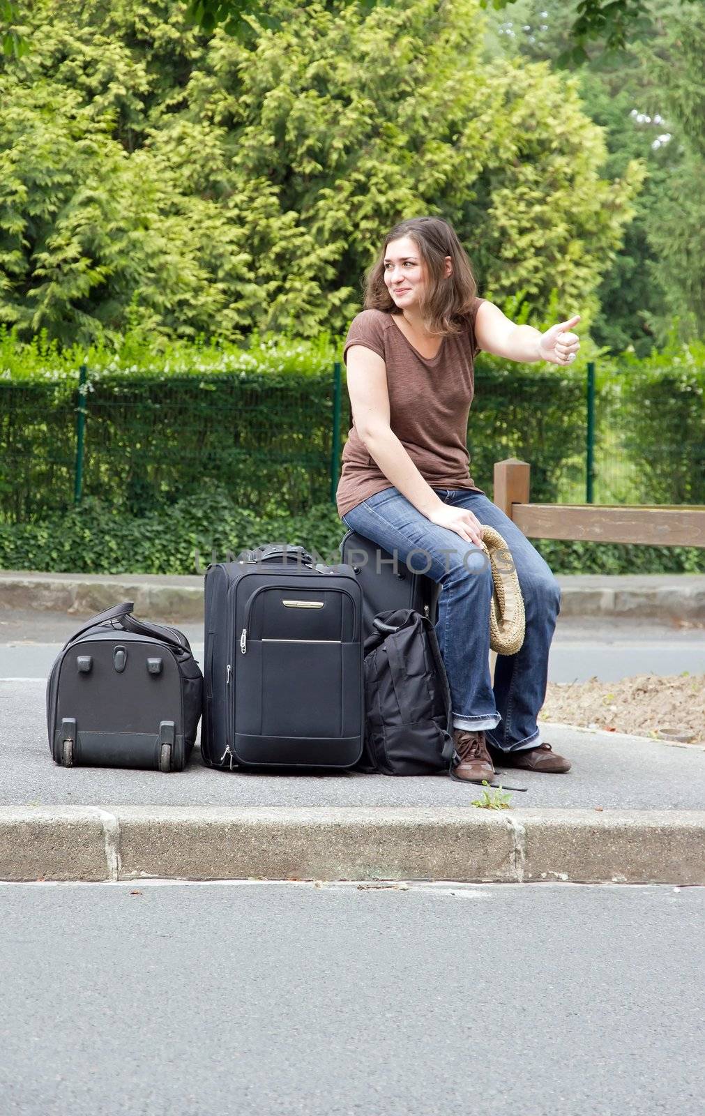 woman making hitchhiking, sitting on his luggage
