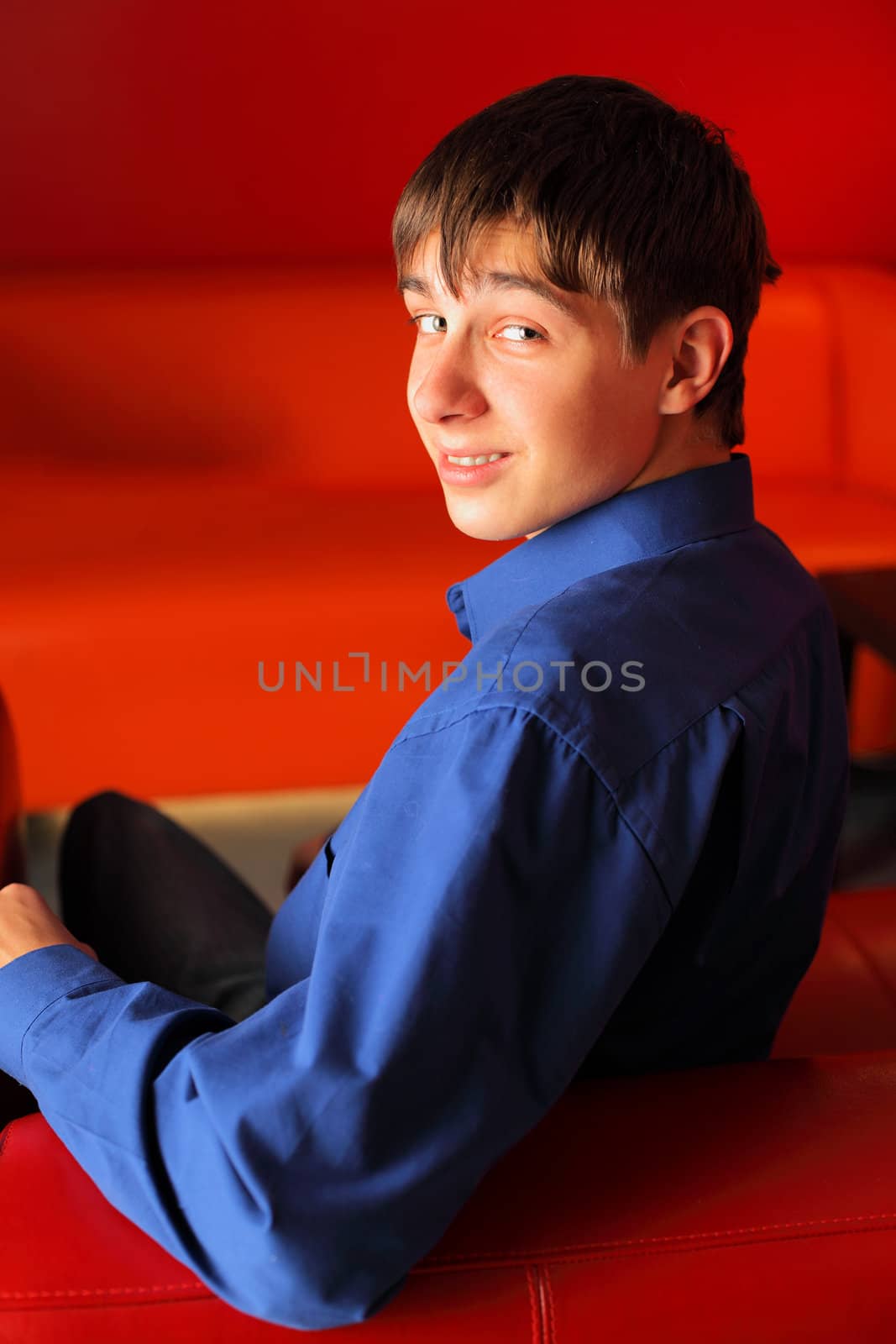 happy teenager sitting on the red sofa in home interior