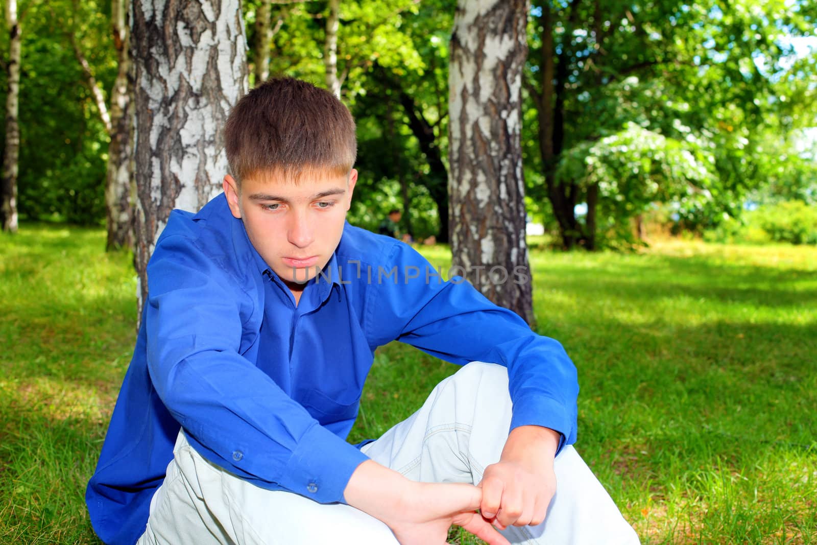 Sad Teenager sitting on the Grass in the Summer Park