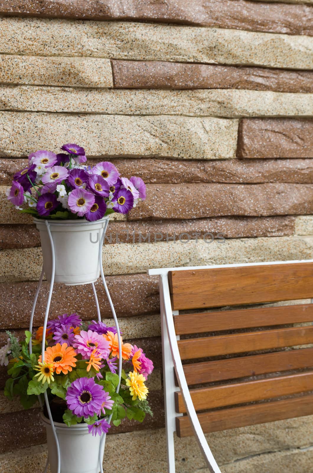 Colorful flowers in white pot wood chair and stone wall