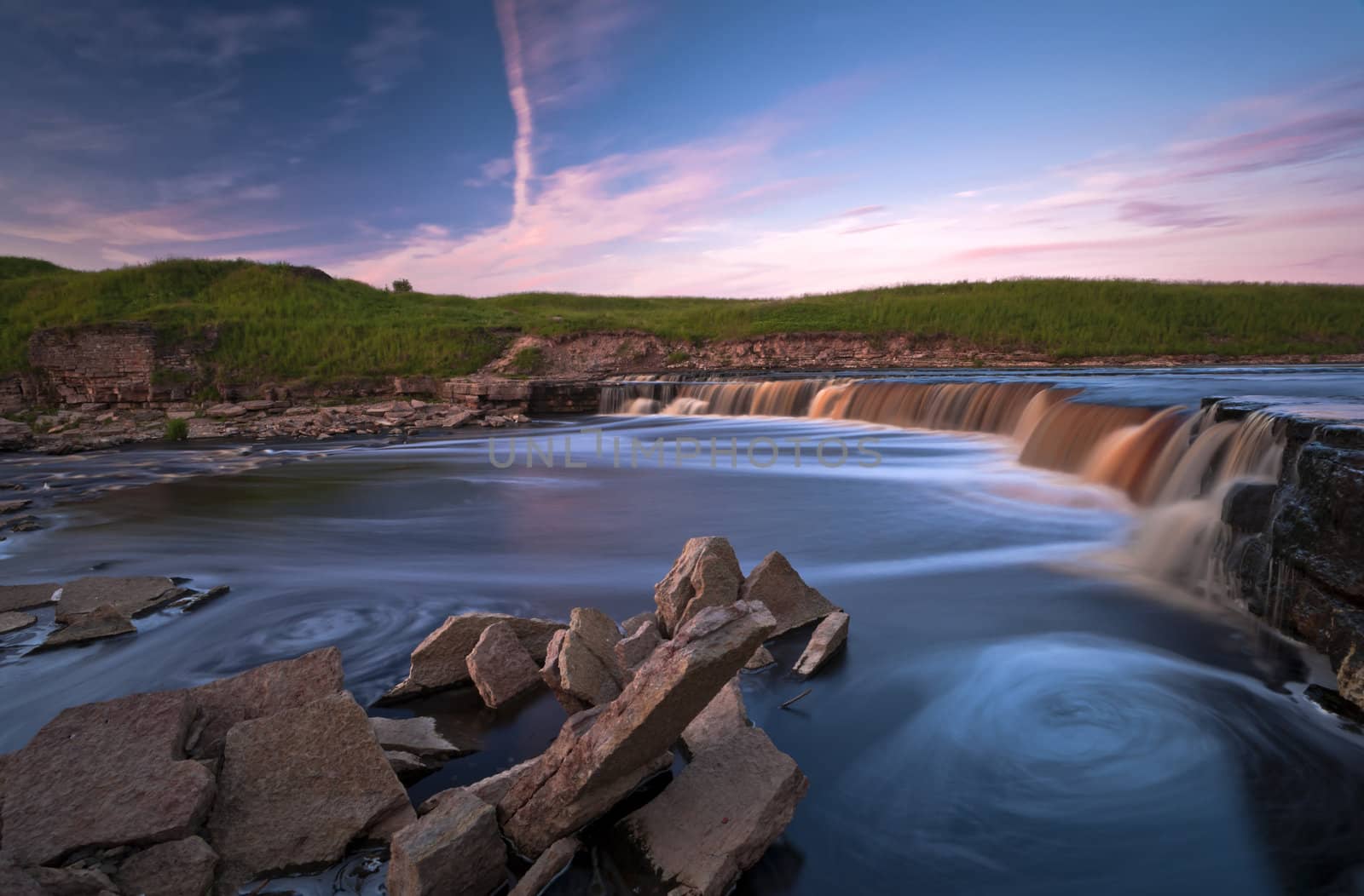 Waterfall of Tosna river with funnels and quarry spalls in sunset light 