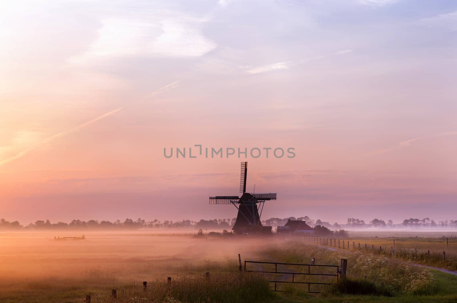 old Dutch windmill in fog in early morning during sunrise