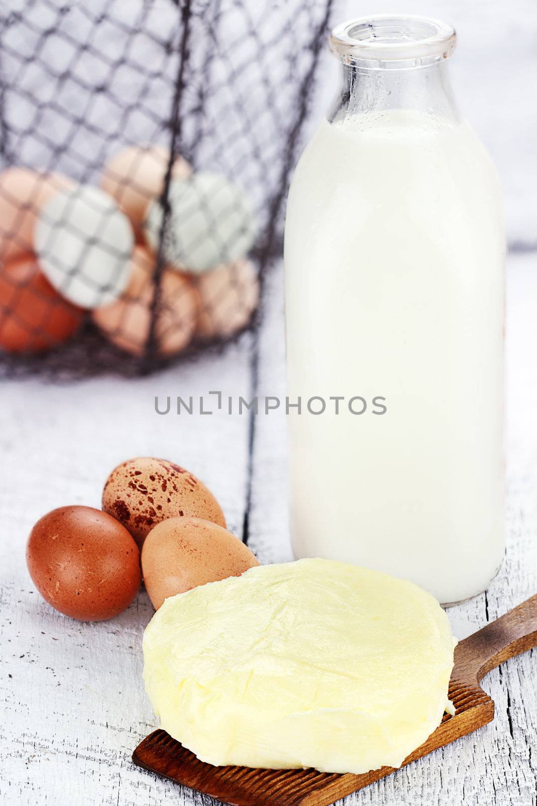 Farm fresh milk, butter, and eggs against a rustic background with basket of eggs. Milk is in a vintage glass milk bottle. Shallow depth of field. 
