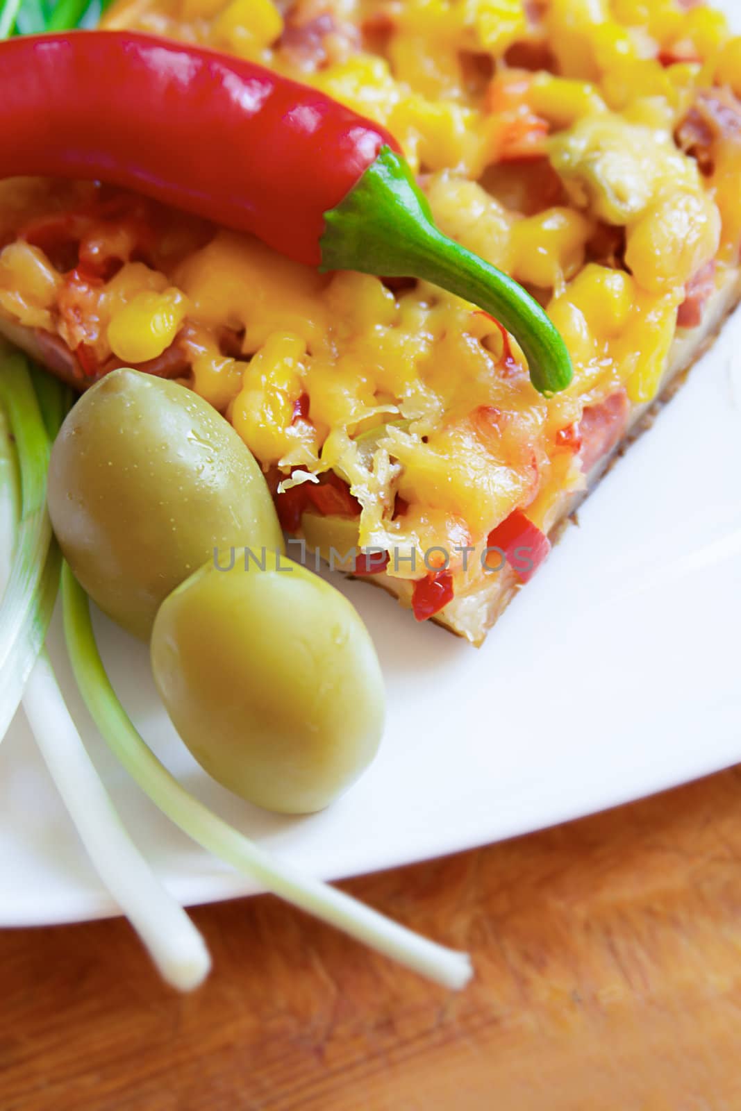 Piece of pizza with chili pepper and olives on plate