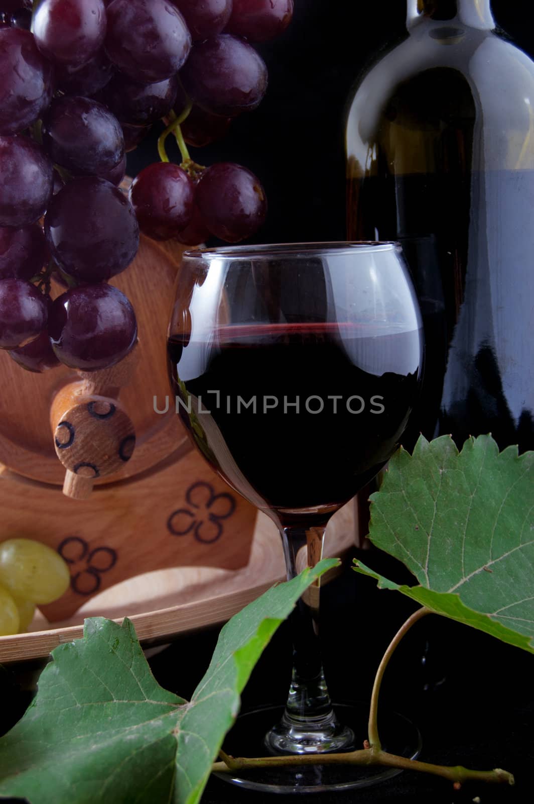 Red wine bottle, glass and cask with grapes over black