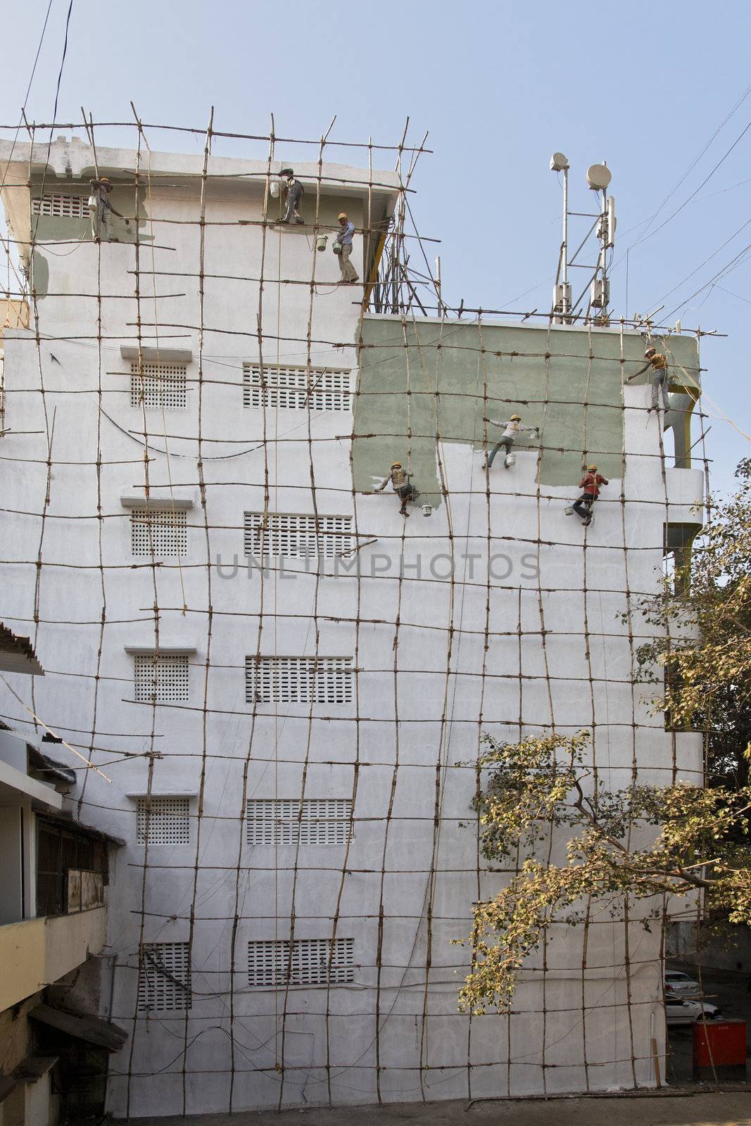 Gang of Indian barefoot Decorators painting exterior of a five story industrial building on a bamboo scaffold